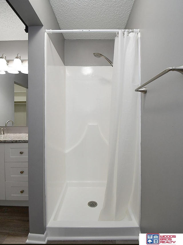 bathroom with a textured ceiling, a stall shower, wood finished floors, and vanity