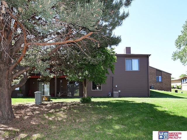 back of house with a yard, a chimney, and central air condition unit