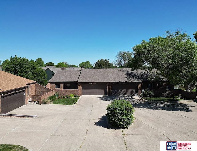 single story home featuring driveway, brick siding, an attached garage, and roof with shingles