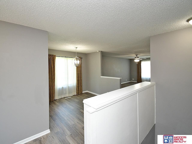 corridor featuring wood finished floors, a textured ceiling, plenty of natural light, and baseboards