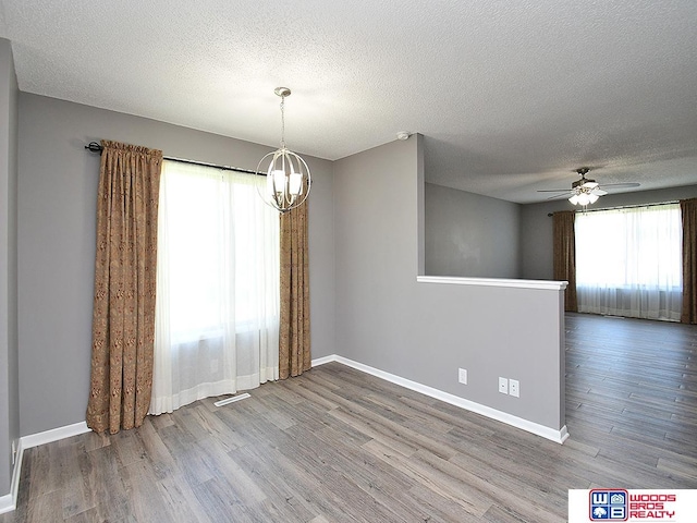 unfurnished room featuring a chandelier, wood finished floors, a textured ceiling, baseboards, and a ceiling fan