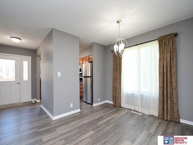 unfurnished dining area featuring wood finished floors, a chandelier, plenty of natural light, a textured ceiling, and baseboards