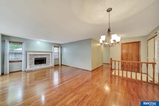 2727 N 75th St, Lincoln, NE 68507 - unfurnished living room featuring a chandelier, light wood finished floors, baseboards, and a stone fireplace