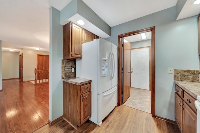 2727 N 75th St, Lincoln, NE 68507 - kitchen featuring white refrigerator with ice dispenser, light wood finished floors, light countertops, tasteful backsplash, and baseboards