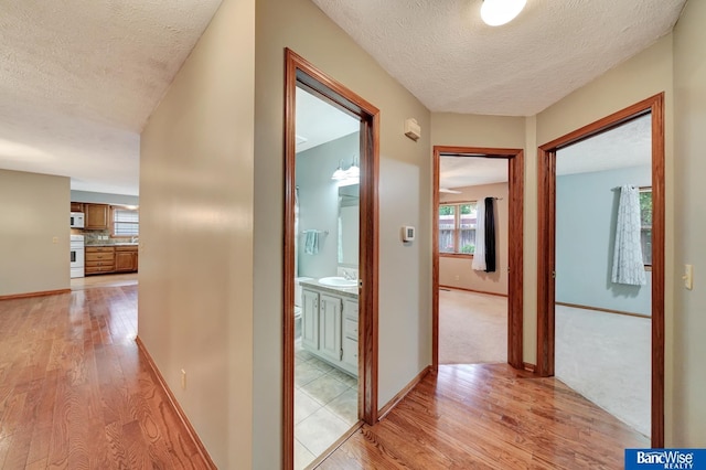 2727 N 75th St, Lincoln, NE 68507 - hallway featuring light wood-type flooring, a textured ceiling, a sink, and baseboards
