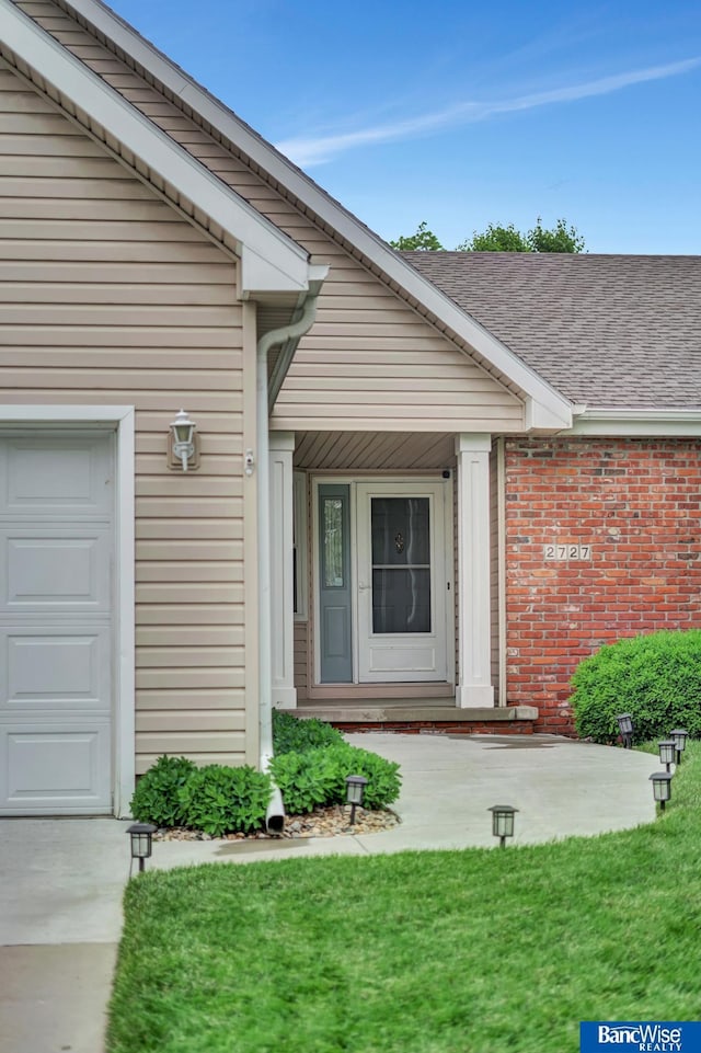 2727 N 75th St, Lincoln, NE 68507 - property entrance featuring an attached garage, roof with shingles, brick siding, and a lawn