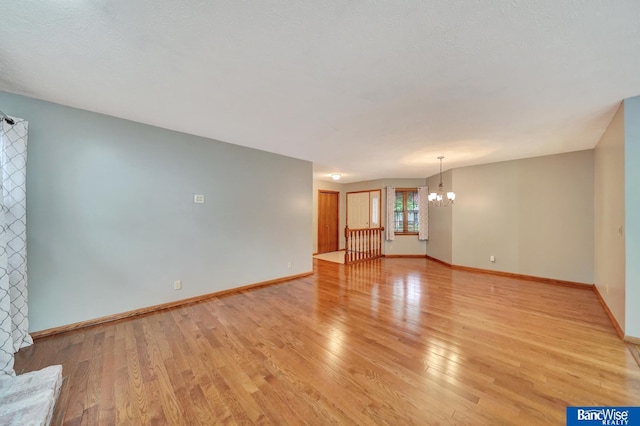 2727 N 75th St, Lincoln, NE 68507 - unfurnished living room with a chandelier, light wood-style flooring, and baseboards