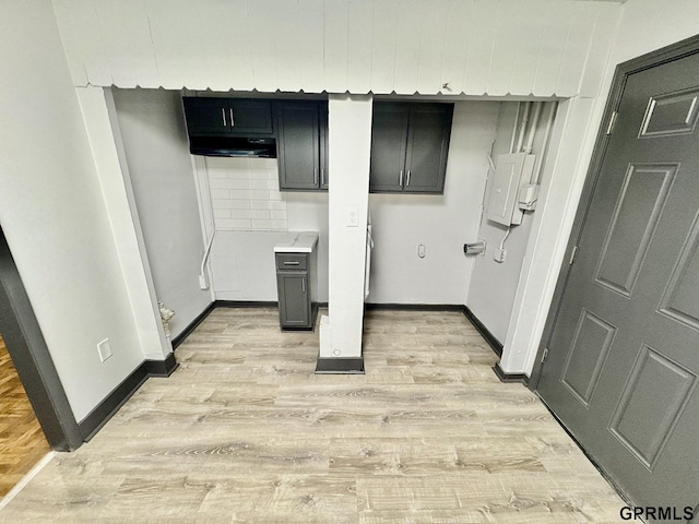 clothes washing area with light wood-style flooring, baseboards, and electric panel