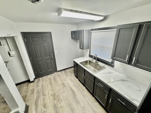 kitchen featuring a sink, light stone counters, light wood-style floors, and dark cabinets