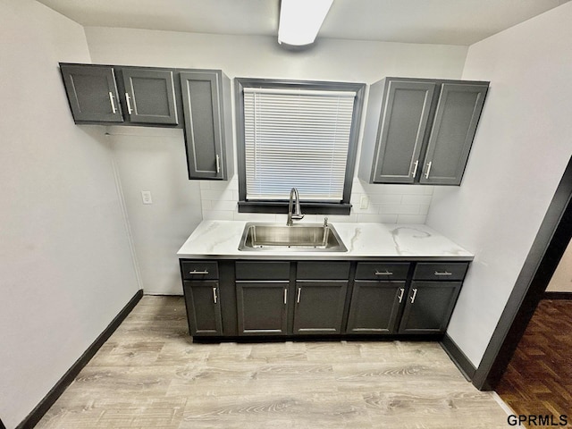 kitchen featuring a sink, light wood-style flooring, decorative backsplash, and baseboards