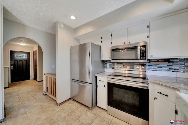 kitchen with stainless steel appliances, arched walkways, tasteful backsplash, white cabinetry, and light tile patterned flooring