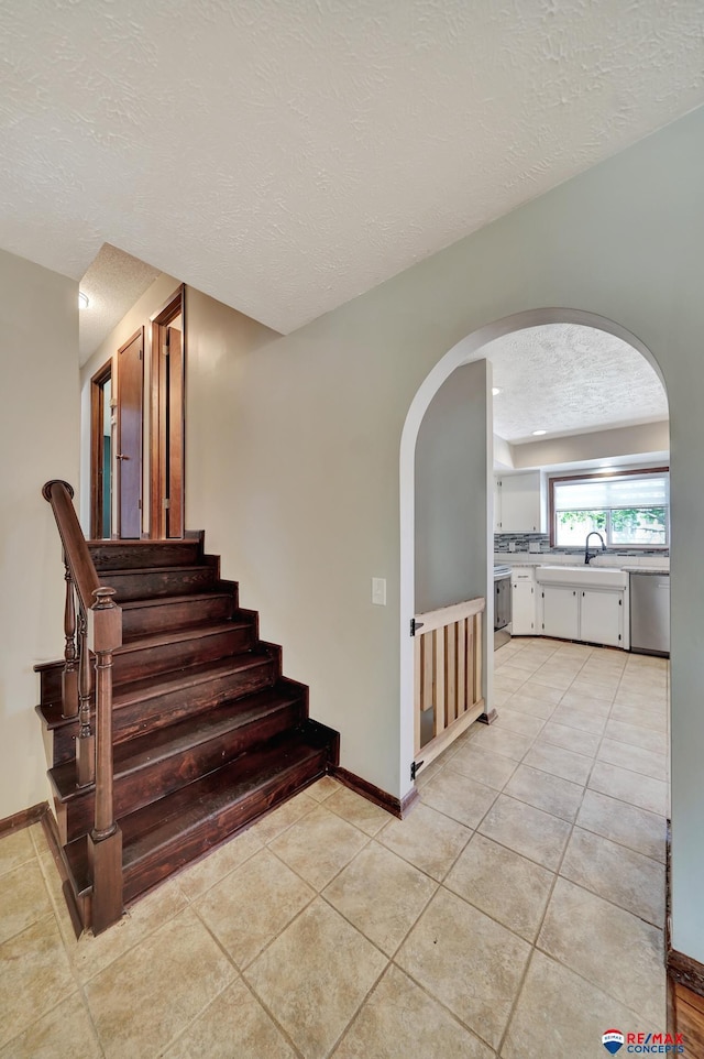 stairway featuring a textured ceiling, arched walkways, baseboards, and tile patterned flooring
