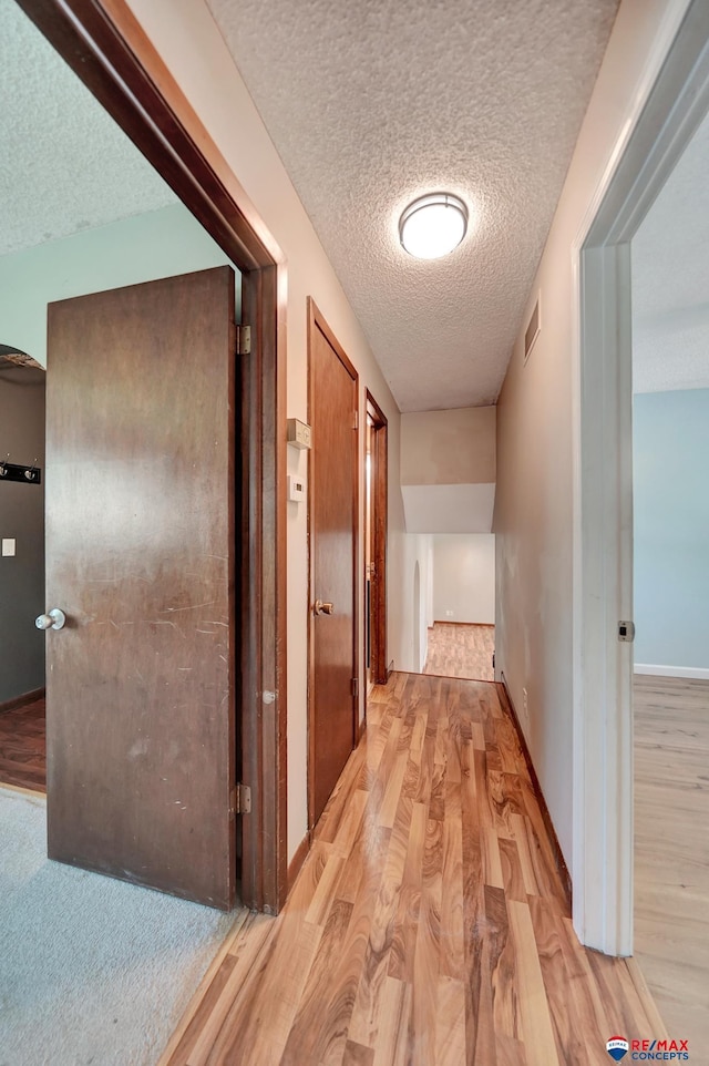 hall with light wood-style floors, a textured ceiling, and baseboards