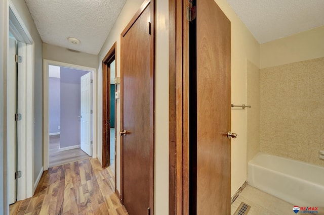 corridor with a textured ceiling, light wood-style flooring, and baseboards