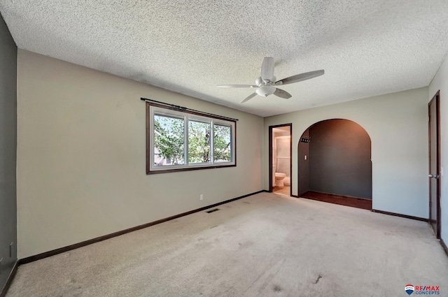 carpeted spare room with a ceiling fan, arched walkways, baseboards, and a textured ceiling