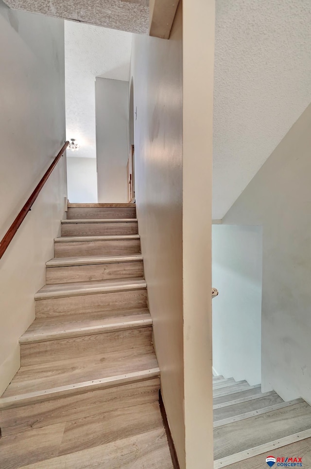 staircase with a textured ceiling and wood finished floors