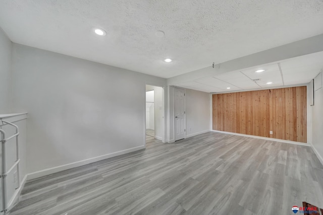 unfurnished living room with baseboards, wood finished floors, wooden walls, recessed lighting, and a textured ceiling