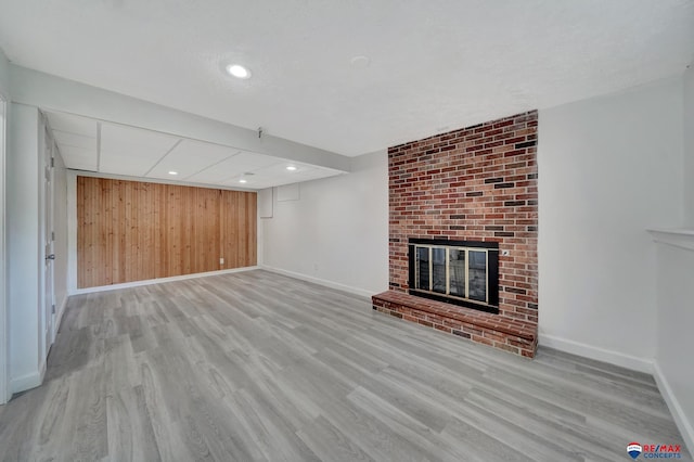 unfurnished living room with a fireplace, baseboards, wood finished floors, wooden walls, and recessed lighting
