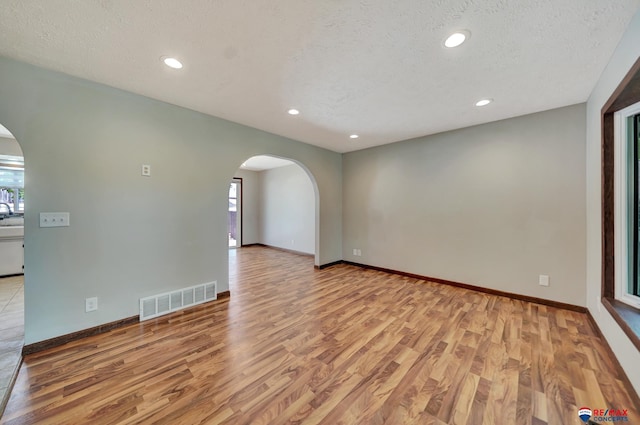 spare room with arched walkways, wood finished floors, plenty of natural light, recessed lighting, and a textured ceiling
