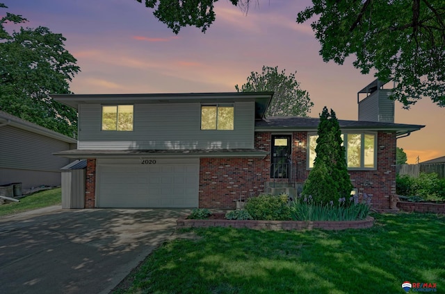 split level home with brick siding, a garage, driveway, and a front yard