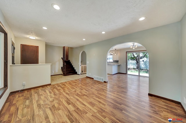 spare room featuring arched walkways, a textured ceiling, light wood-style flooring, a chandelier, and baseboards
