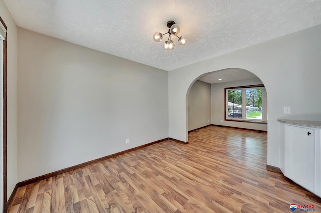 unfurnished dining area featuring arched walkways, light wood-style flooring, baseboards, a textured ceiling, and a chandelier