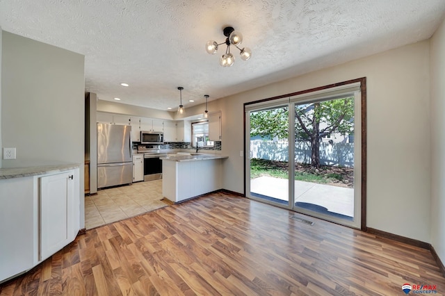 kitchen featuring stainless steel appliances, a peninsula, light wood-type flooring, white cabinetry, and a textured ceiling