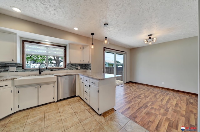 kitchen featuring dishwasher, a sink, a peninsula, backsplash, and white cabinets