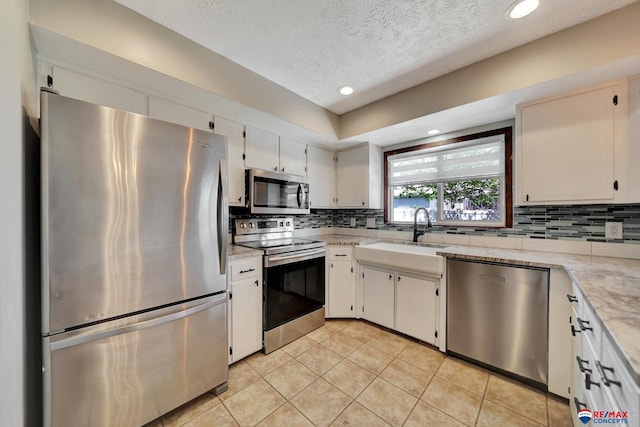 kitchen featuring appliances with stainless steel finishes, a sink, decorative backsplash, light tile patterned floors, and light stone counters