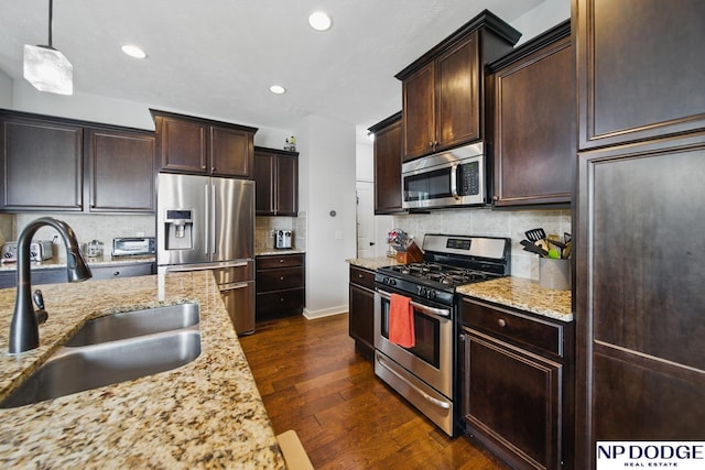 kitchen featuring appliances with stainless steel finishes, a sink, light stone countertops, dark wood-type flooring, and dark brown cabinets
