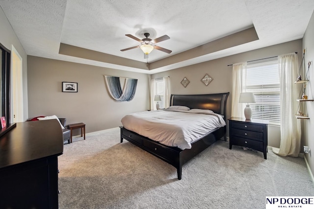 bedroom with a raised ceiling, multiple windows, a textured ceiling, baseboards, and carpet floors