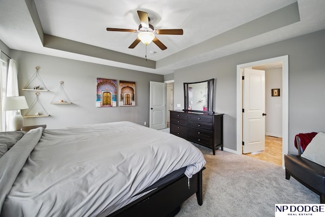 bedroom with a tray ceiling, light colored carpet, baseboards, and ceiling fan