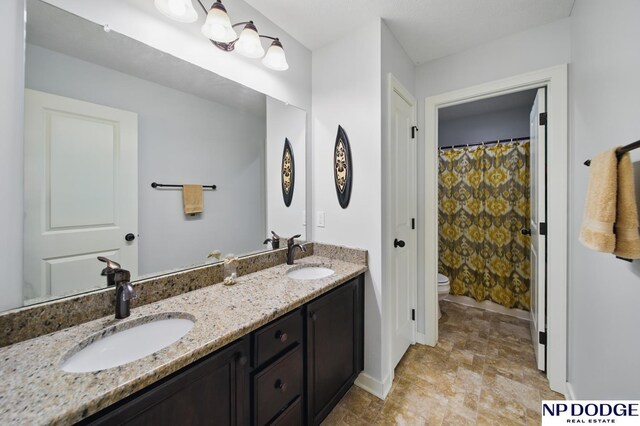 full bathroom featuring double vanity, baseboards, toilet, and stone finish flooring