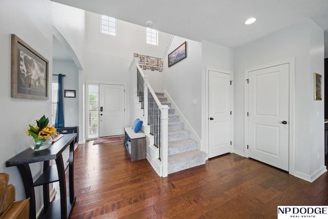 entrance foyer featuring arched walkways, dark wood-type flooring, stairs, recessed lighting, and baseboards