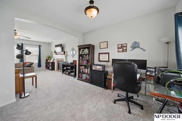 home office with a fireplace, carpet, ceiling fan, and arched walkways