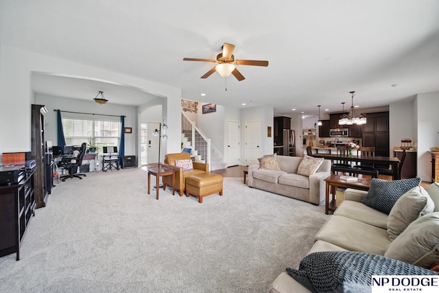 living area featuring ceiling fan, light colored carpet, stairway, a chandelier, and arched walkways