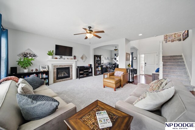 carpeted living area featuring stairway, ceiling fan, arched walkways, and a glass covered fireplace