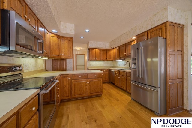 6630 Flint Ridge Rd, Lincoln, NE 68506 - kitchen featuring appliances with stainless steel finishes, a sink, a textured ceiling, light wood-style flooring, and brown cabinets