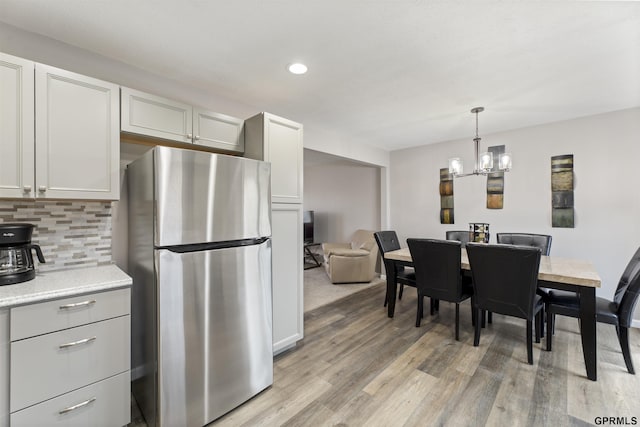 kitchen with freestanding refrigerator, light wood-style flooring, decorative backsplash, light countertops, and a chandelier