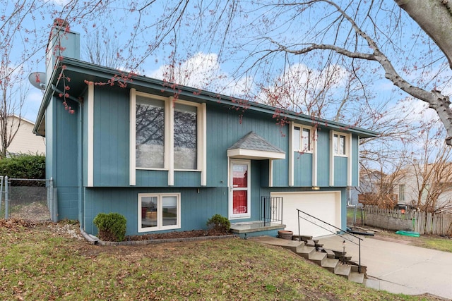 bi-level home featuring concrete driveway, an attached garage, and a chimney