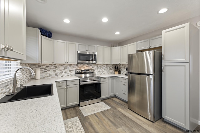 kitchen featuring stainless steel appliances, a sink, light countertops, tasteful backsplash, and wood finished floors