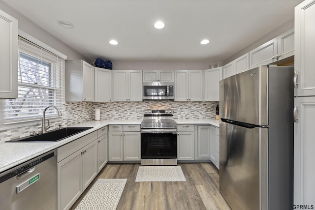 kitchen featuring appliances with stainless steel finishes, a sink, light countertops, light wood-style floors, and backsplash