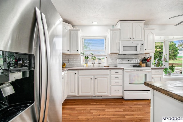kitchen with white appliances, a textured ceiling, a sink, light wood finished floors, and white cabinetry