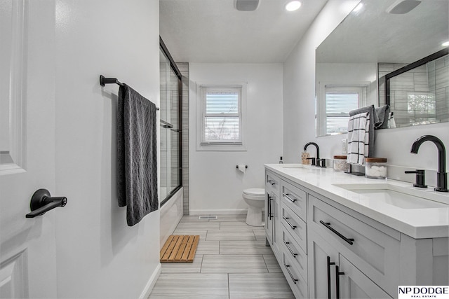 bathroom featuring baseboards, toilet, plenty of natural light, and double vanity