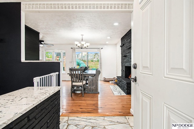 dining area with light wood-style flooring, a chandelier, a fireplace, ceiling fan, and a textured ceiling
