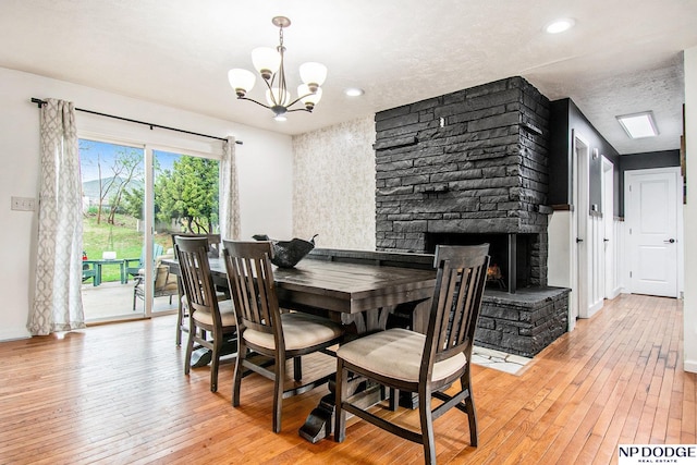 dining room featuring a chandelier, light wood-style floors, a stone fireplace, a textured ceiling, and baseboards