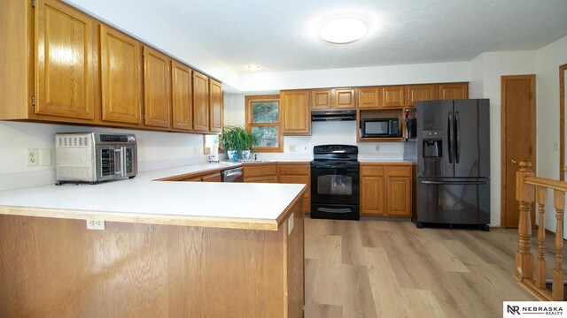 719 Cory Dr, Seward, NE 68434 - kitchen featuring black appliances, under cabinet range hood, light countertops, light wood finished floors, and a peninsula