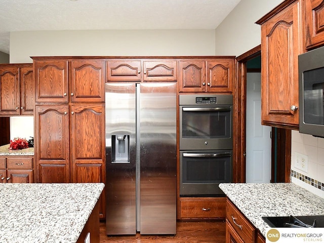 kitchen with stainless steel appliances, light stone counters, dark wood-type flooring, decorative backsplash, and brown cabinets