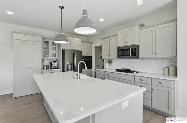 kitchen featuring appliances with stainless steel finishes, decorative backsplash, a center island with sink, light wood finished floors, and recessed lighting