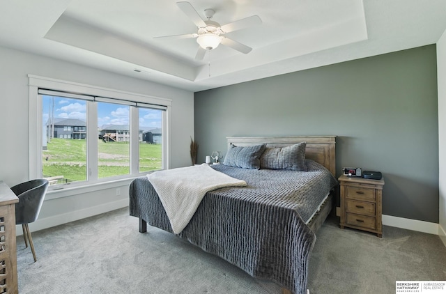 carpeted bedroom featuring a raised ceiling, baseboards, and ceiling fan